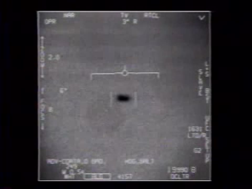 Frame do vídeo FLIR1 mostrando um objeto oblongo escuro ao centro da mira de um sensor infravermelho militar