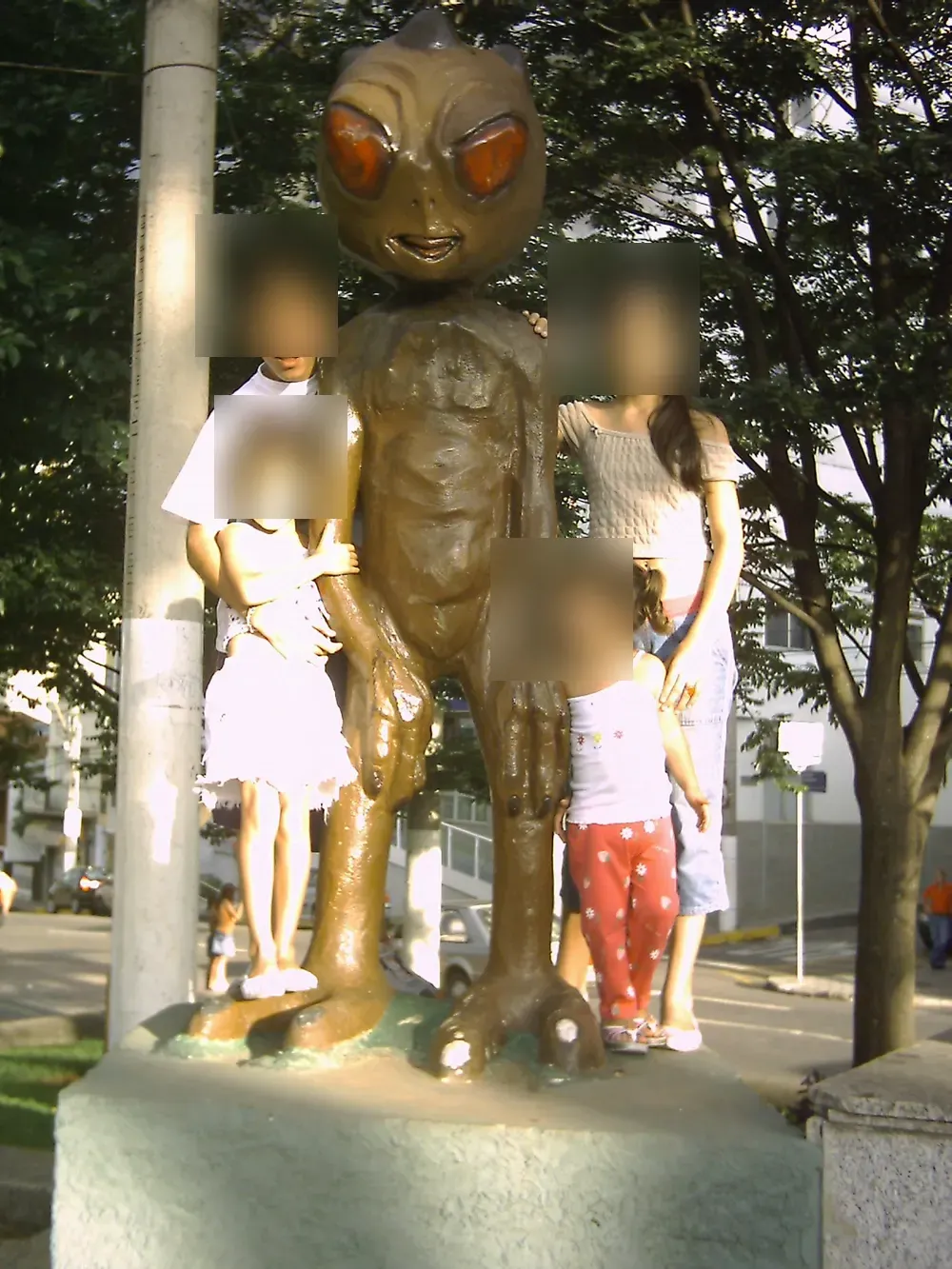 Escultura do ET de Varginha em um cruzamento da cidade, fotografada em 2009; rostos de crianças borrados para preservar a privacidade